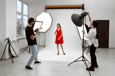 Photo of Professional photographer and assistant working with beautiful model in modern photo studio