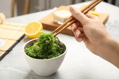 Photo of Woman eating Japanese seaweed salad at light marble table, closeup