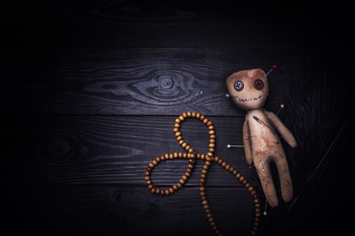 Image of Voodoo doll pierced with pins, beads and feather on black wooden table, flat lay