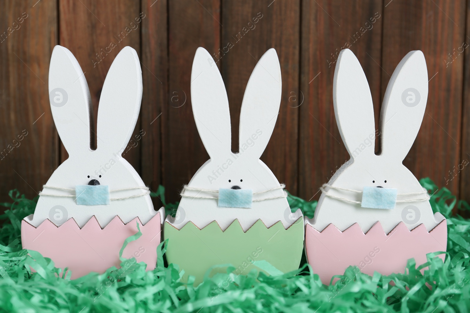 Photo of Cute bunny figures in protective masks on wooden background. Easter holiday during COVID-19 quarantine