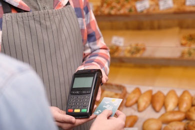 Photo of Woman using credit card for terminal payment in bakery, closeup. Space for text