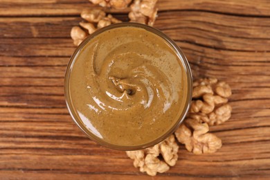 Delicious nut butter in bowl and walnuts on wooden table, top view