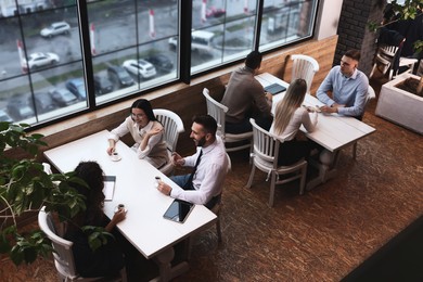Photo of Coworkers having coffee break near window in cafe, above view