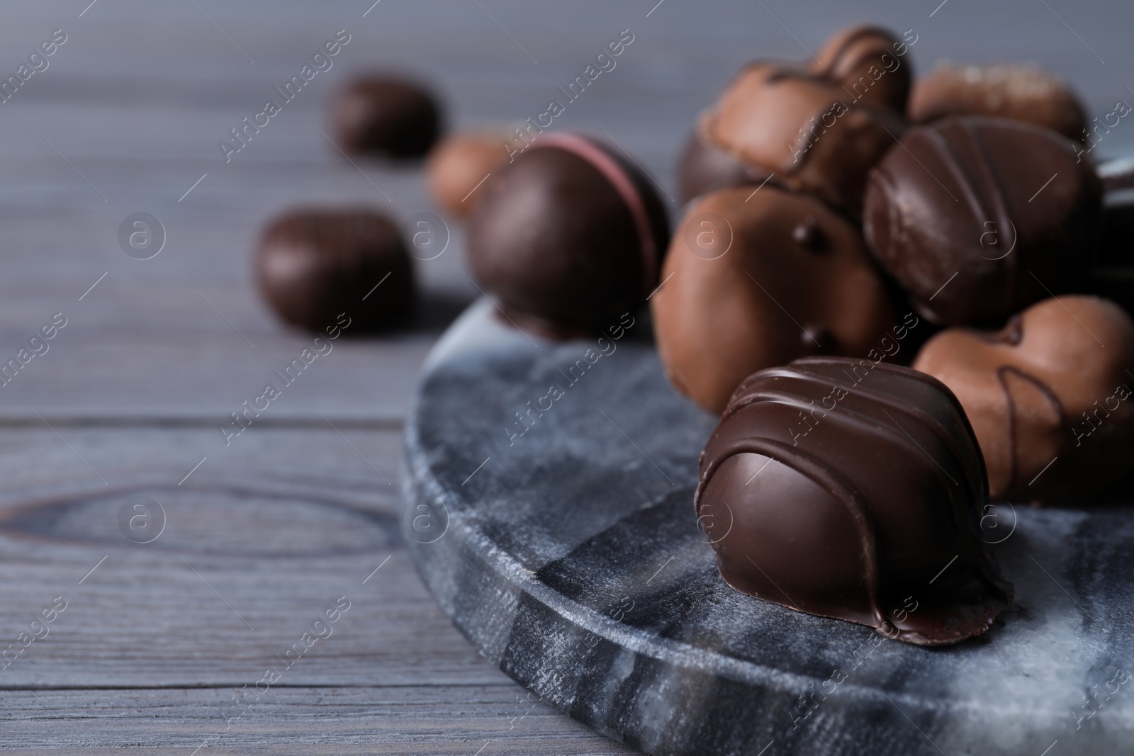 Photo of Tasty chocolate candies on grey marble board closeup. Space for text