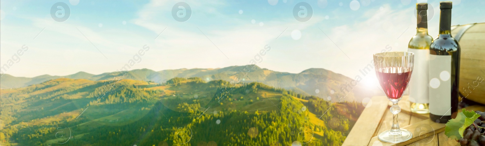 Image of Tasty wine and grapes on wooden table against beautiful mountain landscape, space for text. Banner design