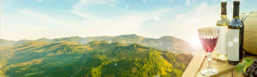 Tasty wine and grapes on wooden table against beautiful mountain landscape, space for text. Banner design