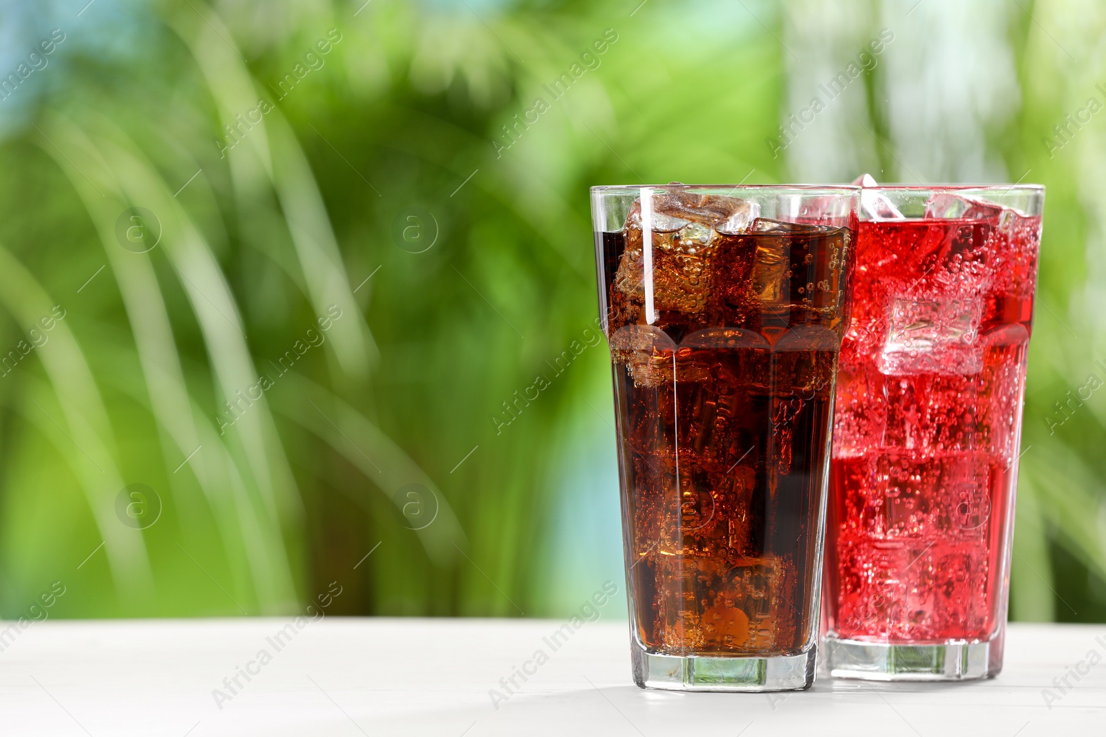 Photo of Glasses of different refreshing soda water with ice cubes on white table outdoors, space for text