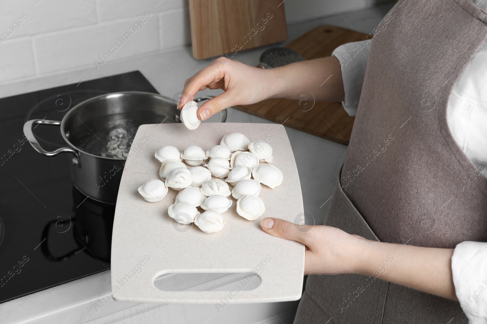 Photo of Woman putting frozen dumplings into saucepan with boiling water on cooktop in kitchen, closeup