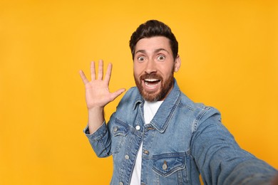 Funny bearded man taking selfie on orange background
