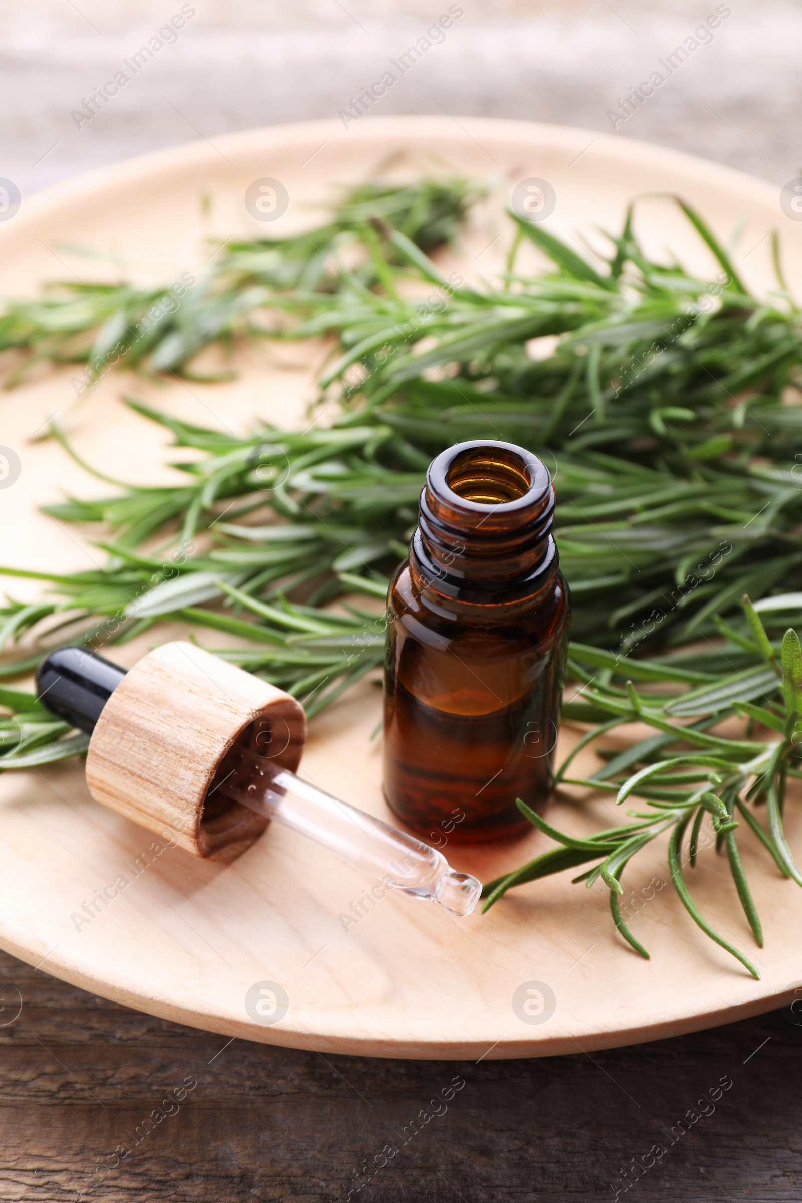 Photo of Bottle of rosemary essential oil and pipette on wooden table, closeup