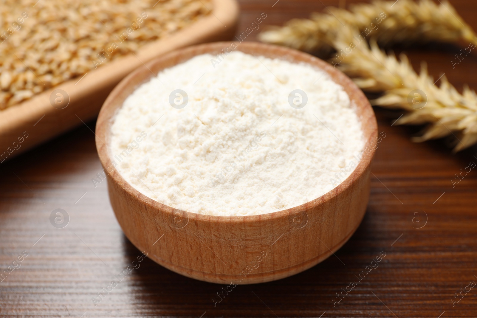 Photo of Wheat flour in bowl on wooden table, closeup