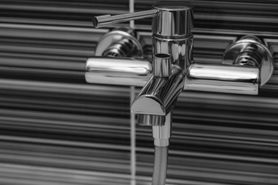 Photo of Shiny bath water tap installed on black and white wall, space for text