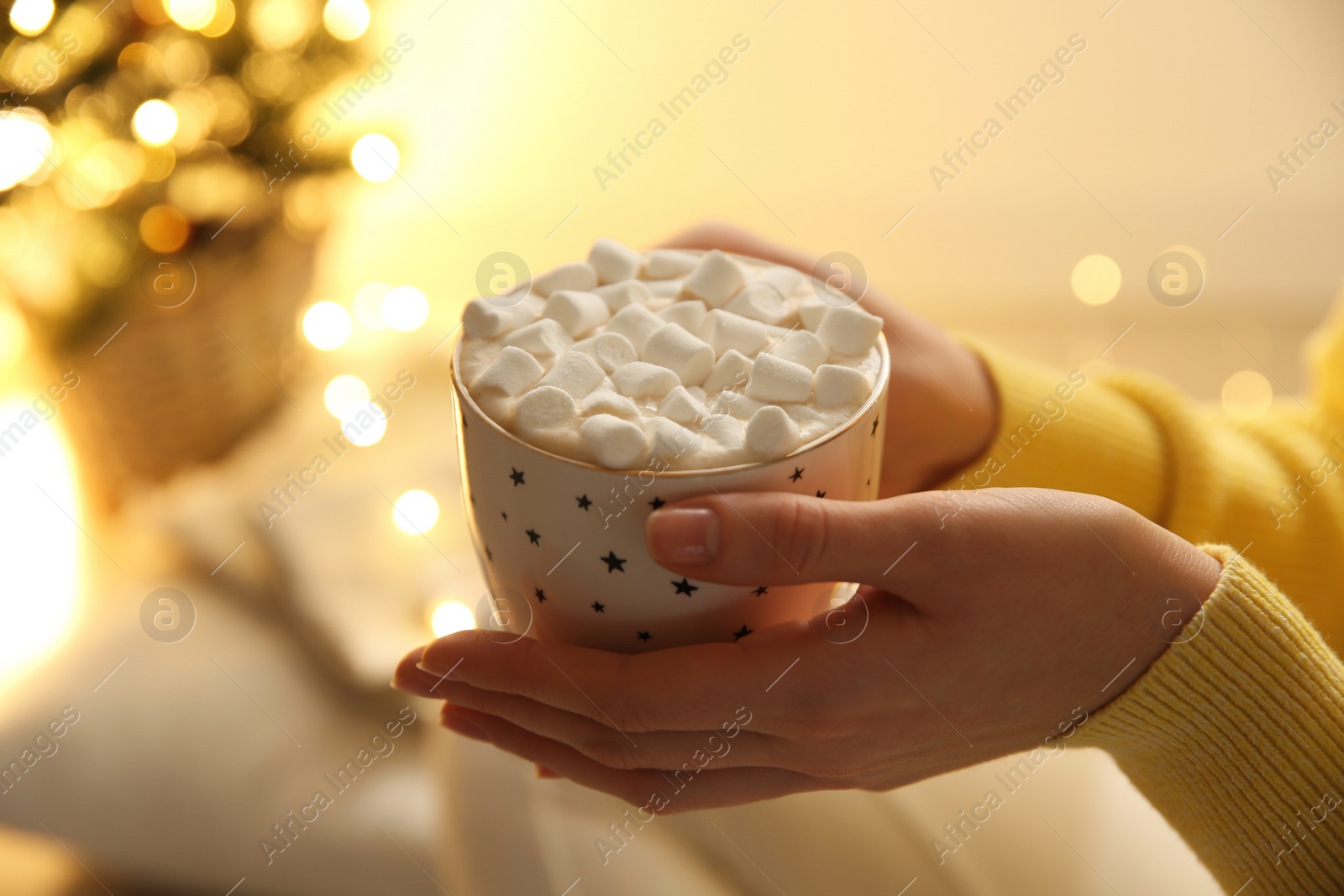 Photo of Woman holding cup of hot drink with marshmallow indoors, closeup