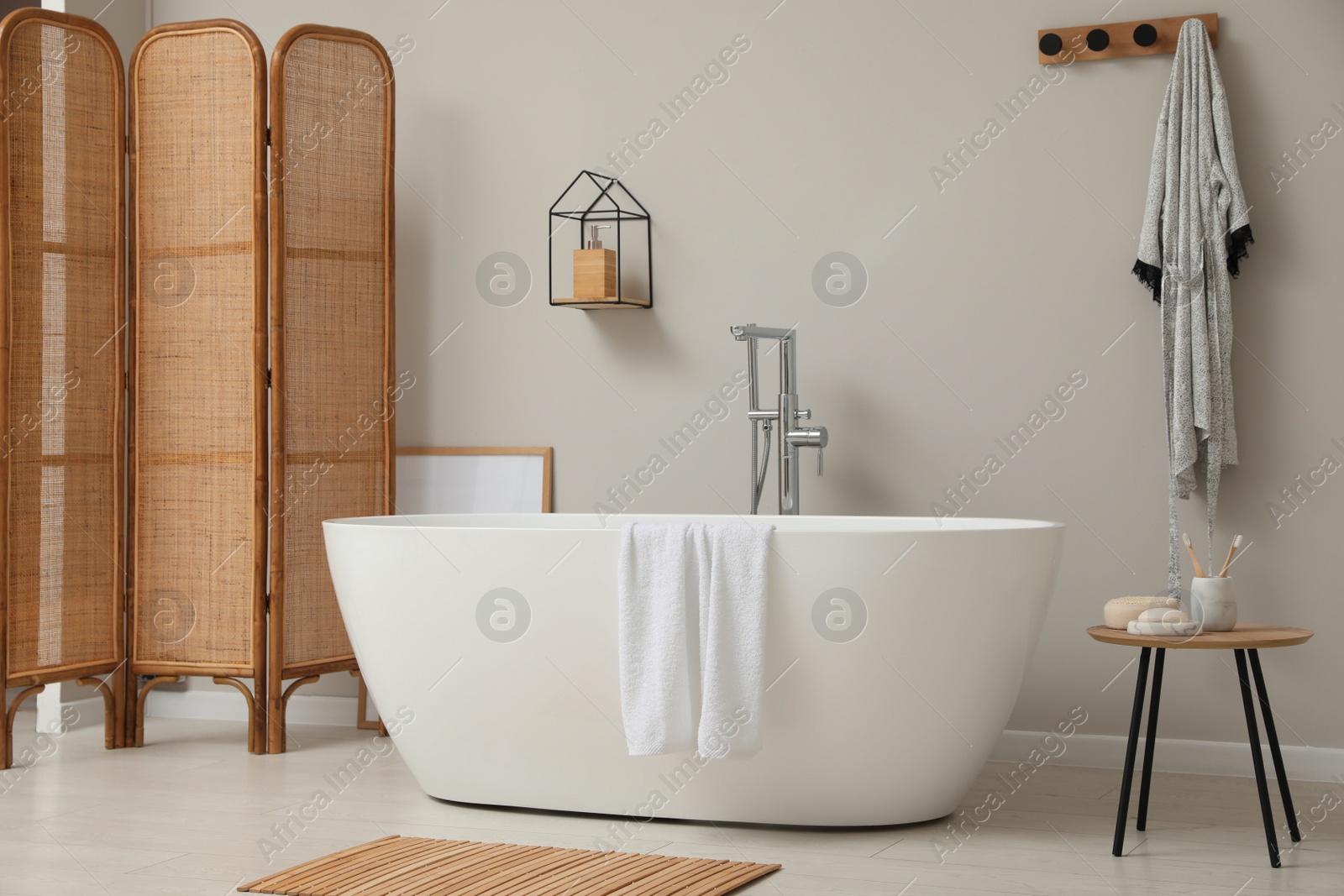 Photo of Modern ceramic bathtub and folding screen near white wall in room