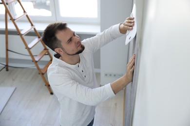 Photo of Man smoothing stylish gray wallpaper in room