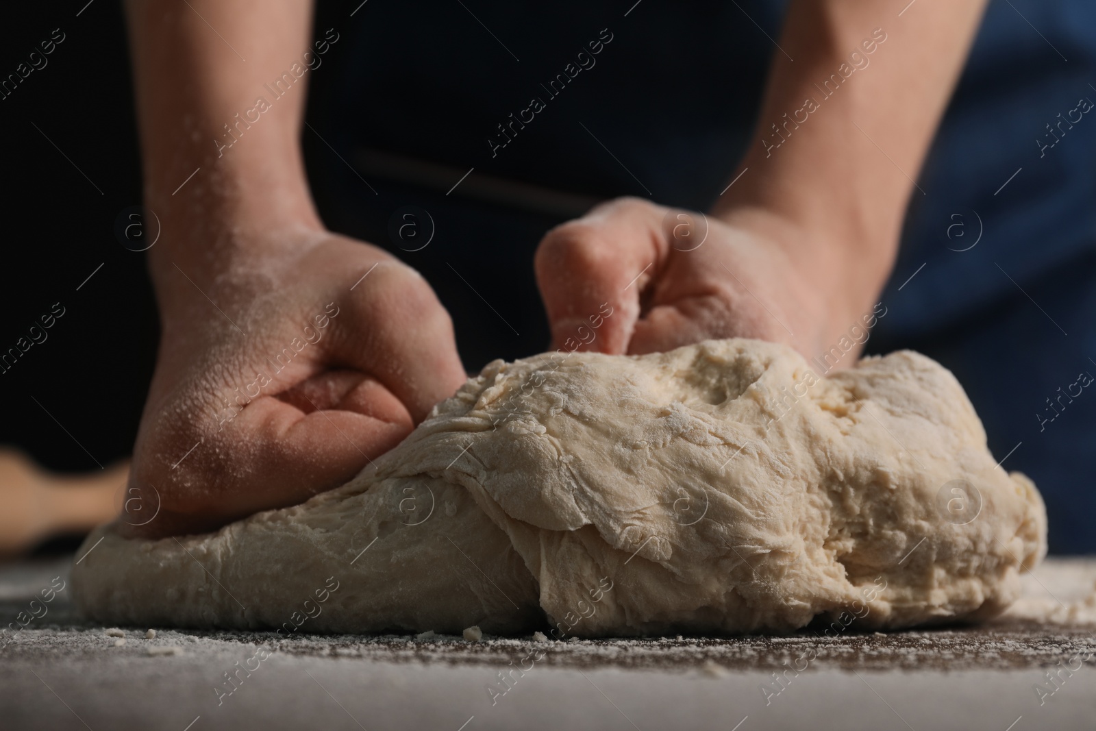 Photo of Making bread. Woman kneading dough at table on dark background, closeup