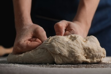 Photo of Making bread. Woman kneading dough at table on dark background, closeup