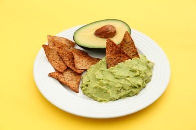 Photo of Delicious guacamole, avocado and nachos on yellow background