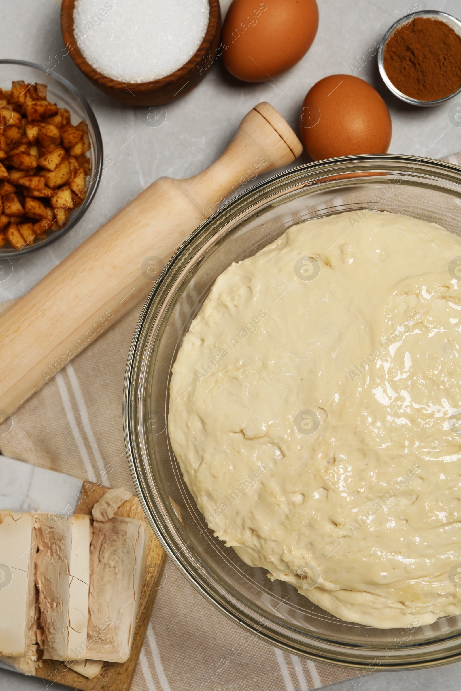 Photo of Fresh yeast dough in glass bowl and ingredient for cake on marble table, flat lay