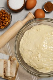 Fresh yeast dough in glass bowl and ingredient for cake on marble table, flat lay