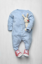 Photo of Child's bodysuit with booties and toy bunny on white wooden background, flat lay
