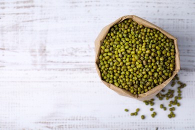 Photo of Paper bag with green mung beans on white wooden table, top view. Space for text