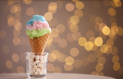 Photo of Sweet cotton candy in waffle cone on table against blurred lights, closeup. Space for text