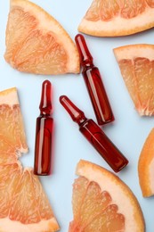 Skincare ampoules with vitamin C and slices of grapefruit on light blue background, flat lay