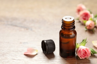 Photo of Bottle of rose essential oil and fresh flowers on wooden table, space for text