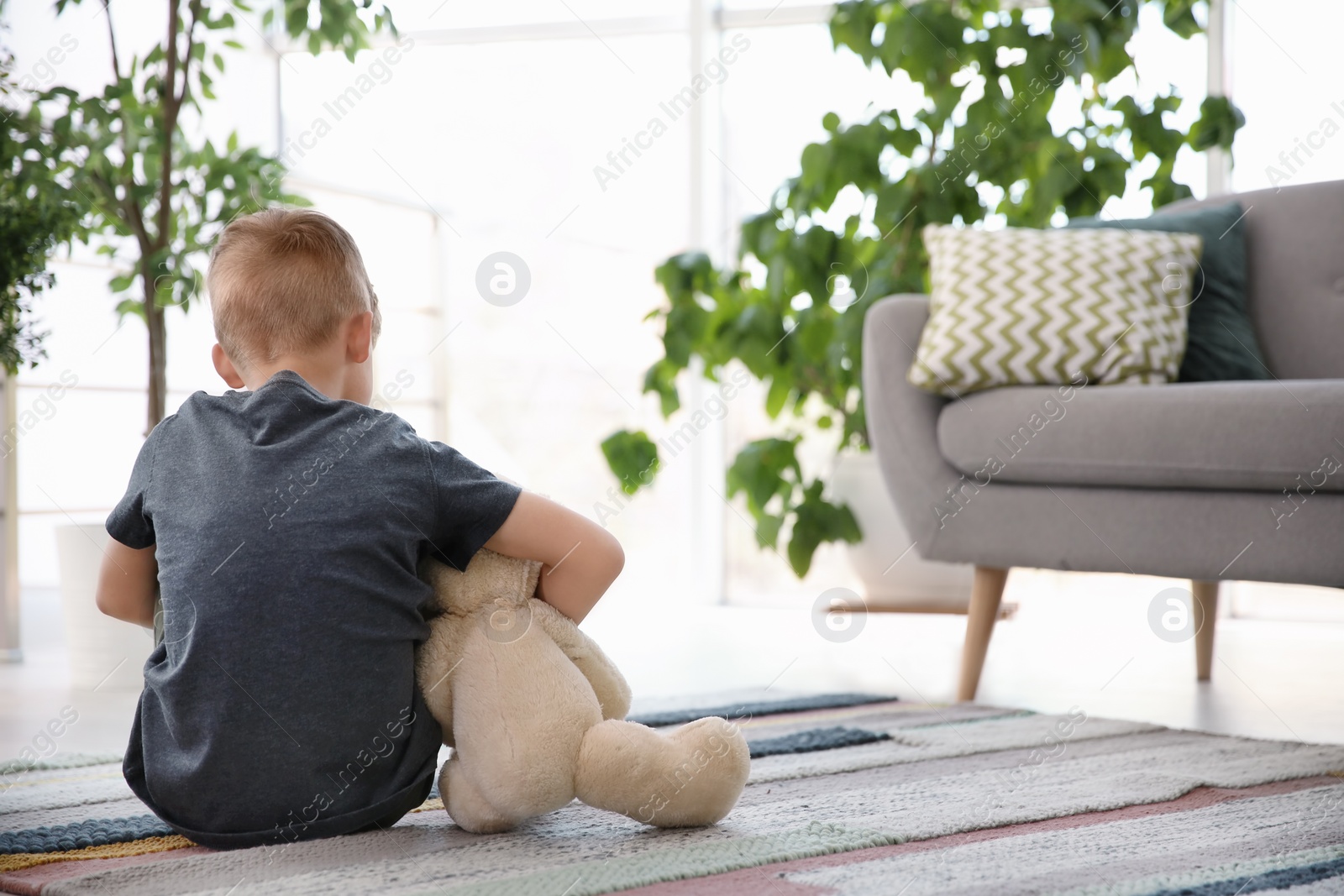 Photo of Lonely little boy with teddy bear sitting on floor at home. Autism concept