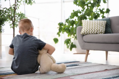 Photo of Lonely little boy with teddy bear sitting on floor at home. Autism concept