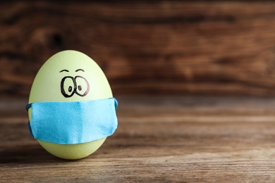 Bright egg in protective mask on wooden table, space for text. Easter holiday during coronavirus quarantine