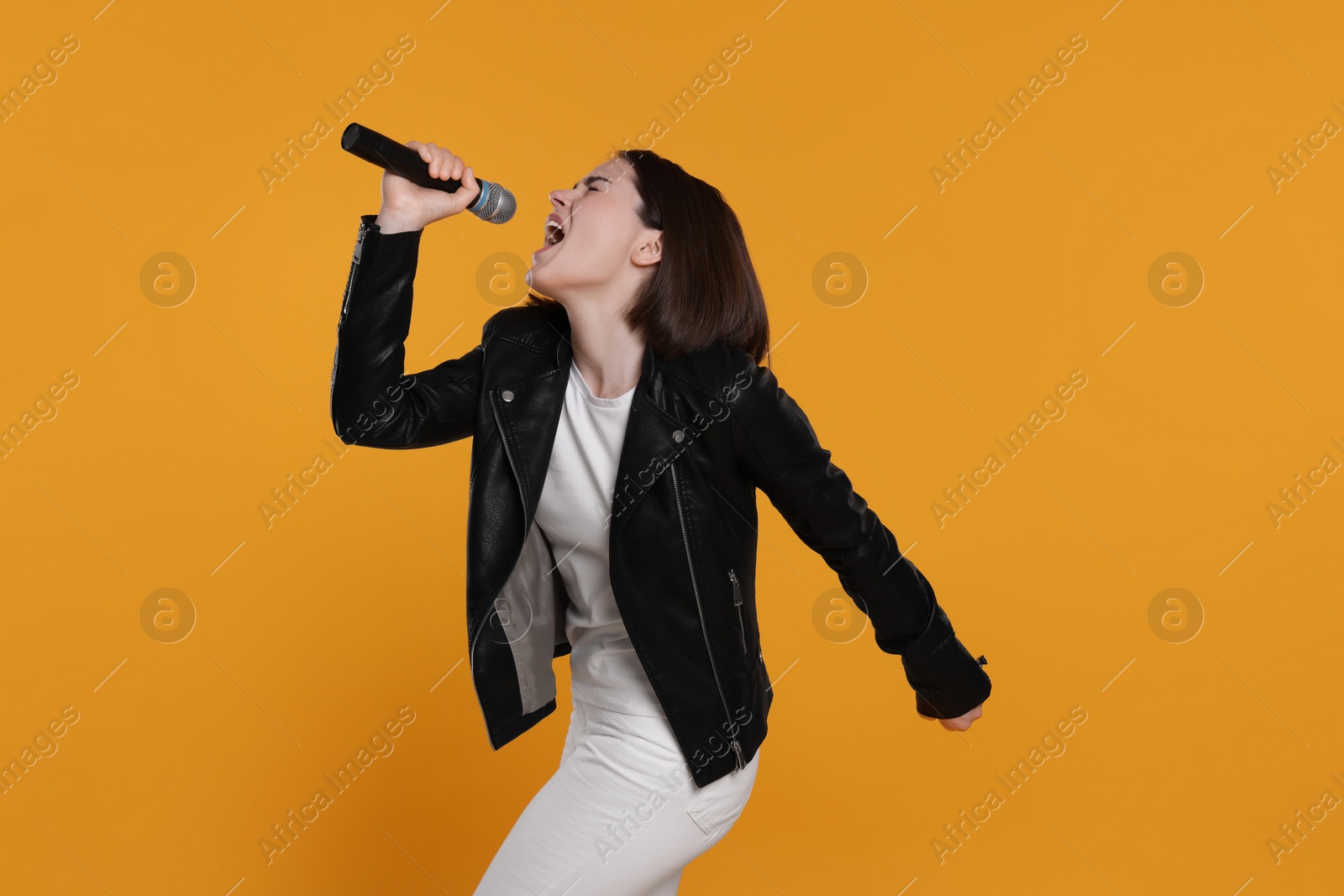 Photo of Beautiful young woman with microphone singing on yellow background