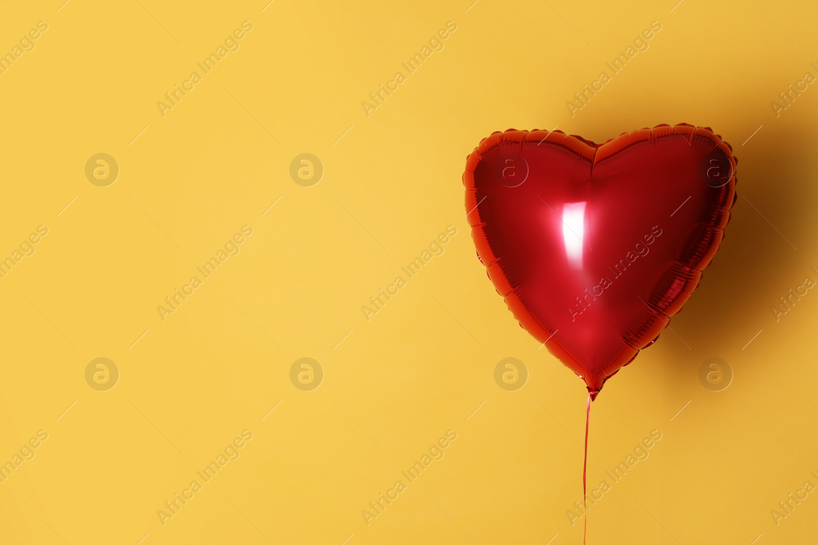 Photo of Festive heart shaped balloon on yellow background. Space for text