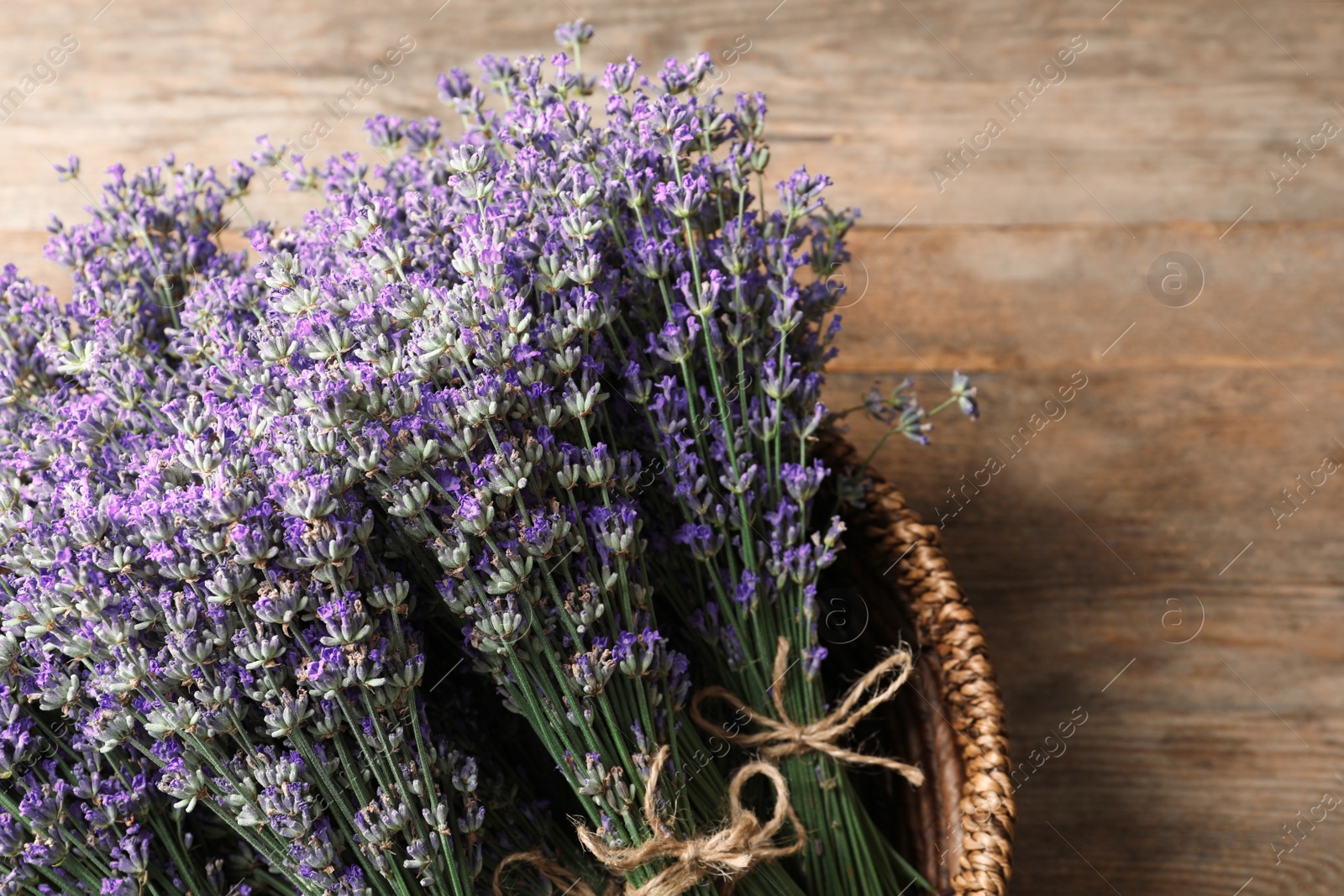 Photo of Fresh lavender flowers in basket on wooden table, closeup. Space for text