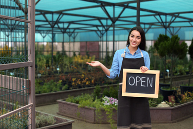 Female business owner holding OPEN sign in greenhouse. Space for text