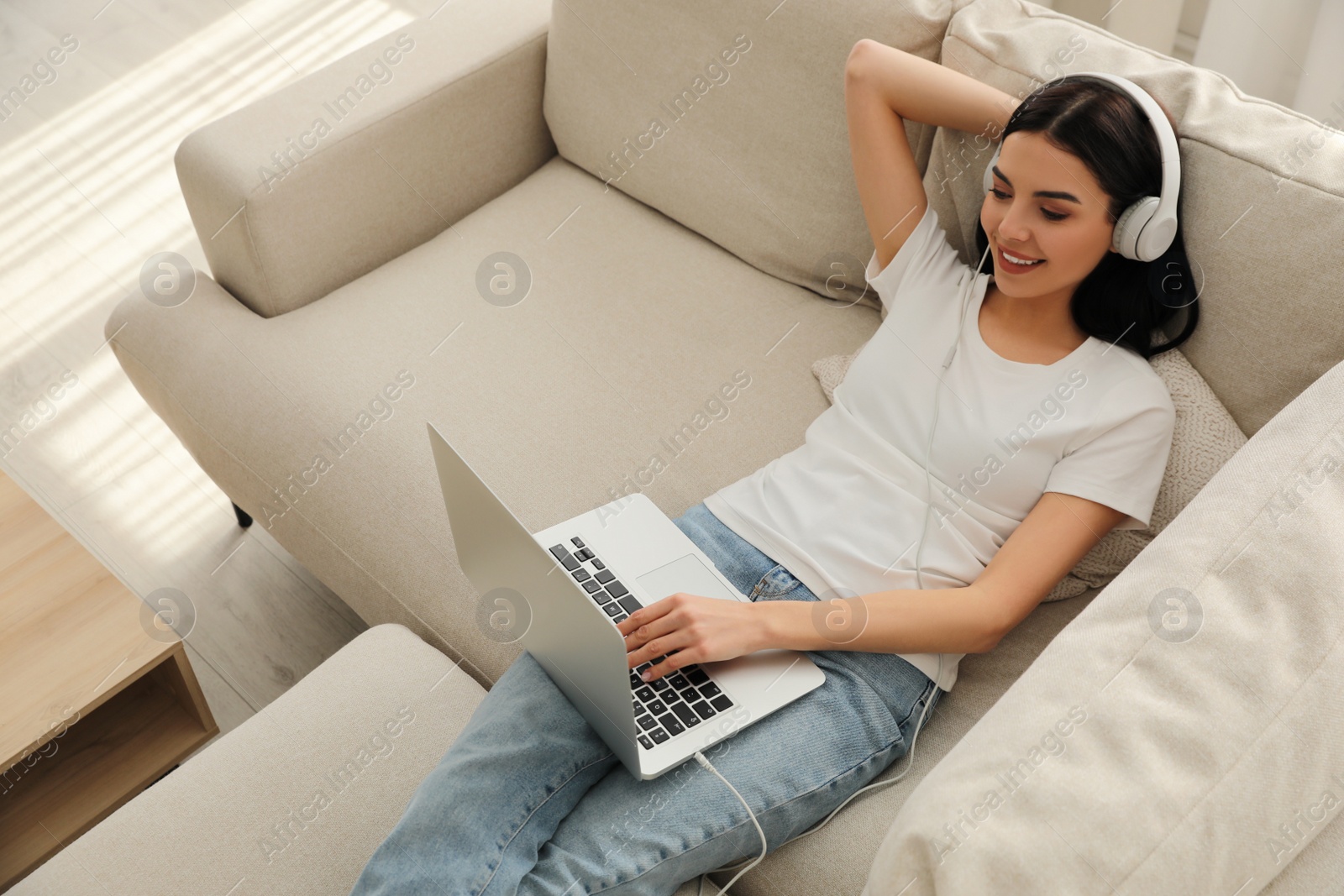 Photo of Woman with laptop and headphones lying on sofa at home