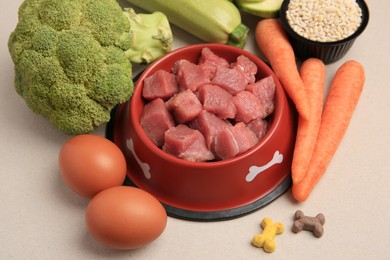 Raw meat in bowl, products and vitamins for pet on beige background