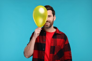 Happy man with yellow balloon on light blue background