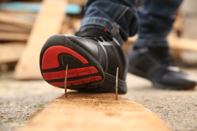 Photo of Careless worker stepping on nail in wooden plank outdoors, closeup