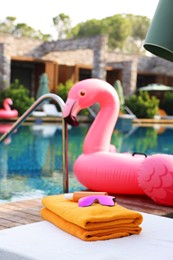 Photo of Beach accessories on sun lounger and float in shape of flamingo near outdoor swimming pool. Luxury resort