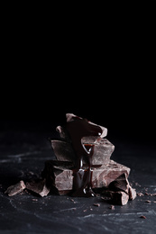 Photo of Pieces of tasty dark chocolate with syrup on black table, closeup. Space for text