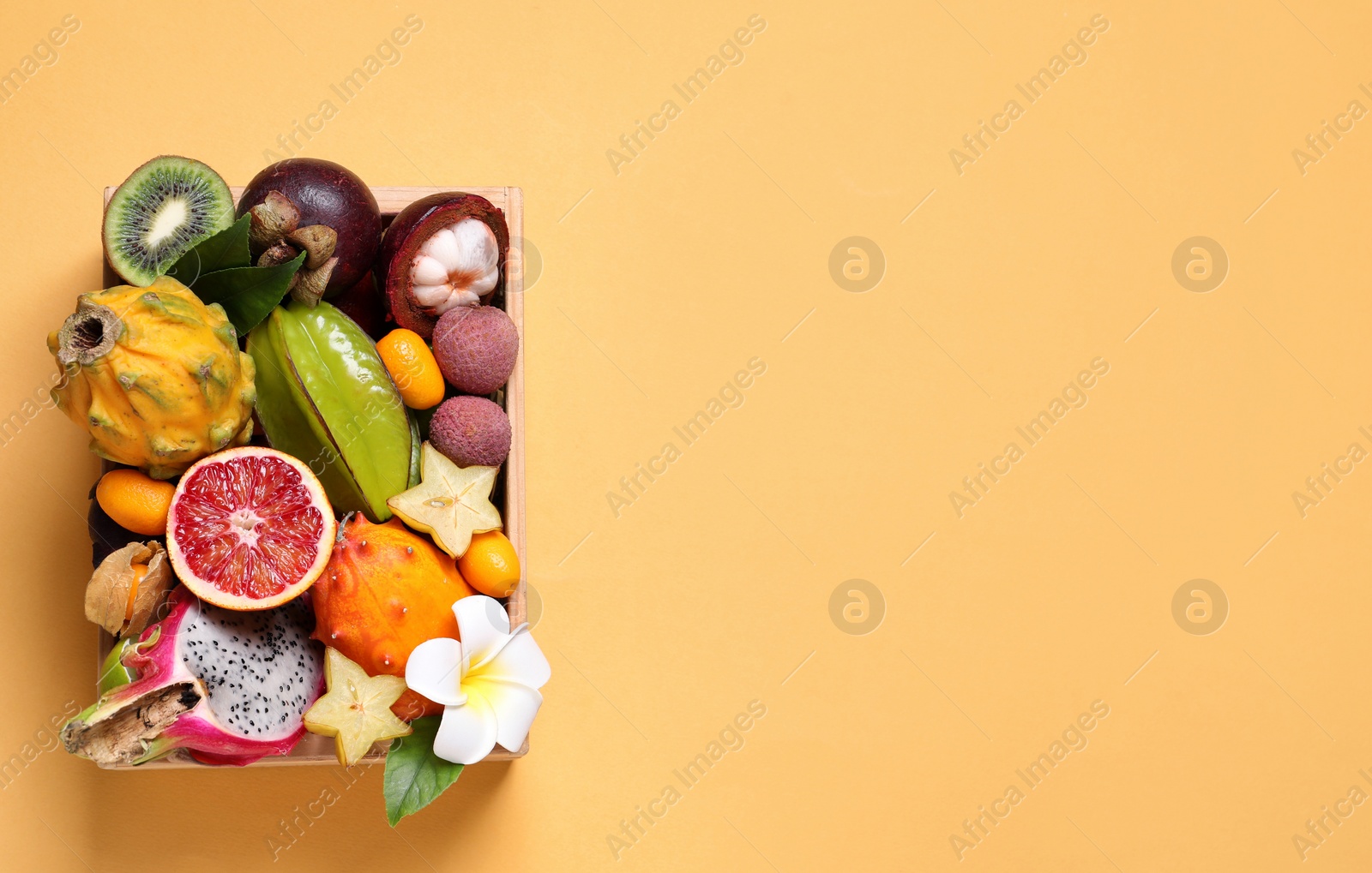Photo of Different tropical fruits in wooden box on yellow background, top view. Space for text