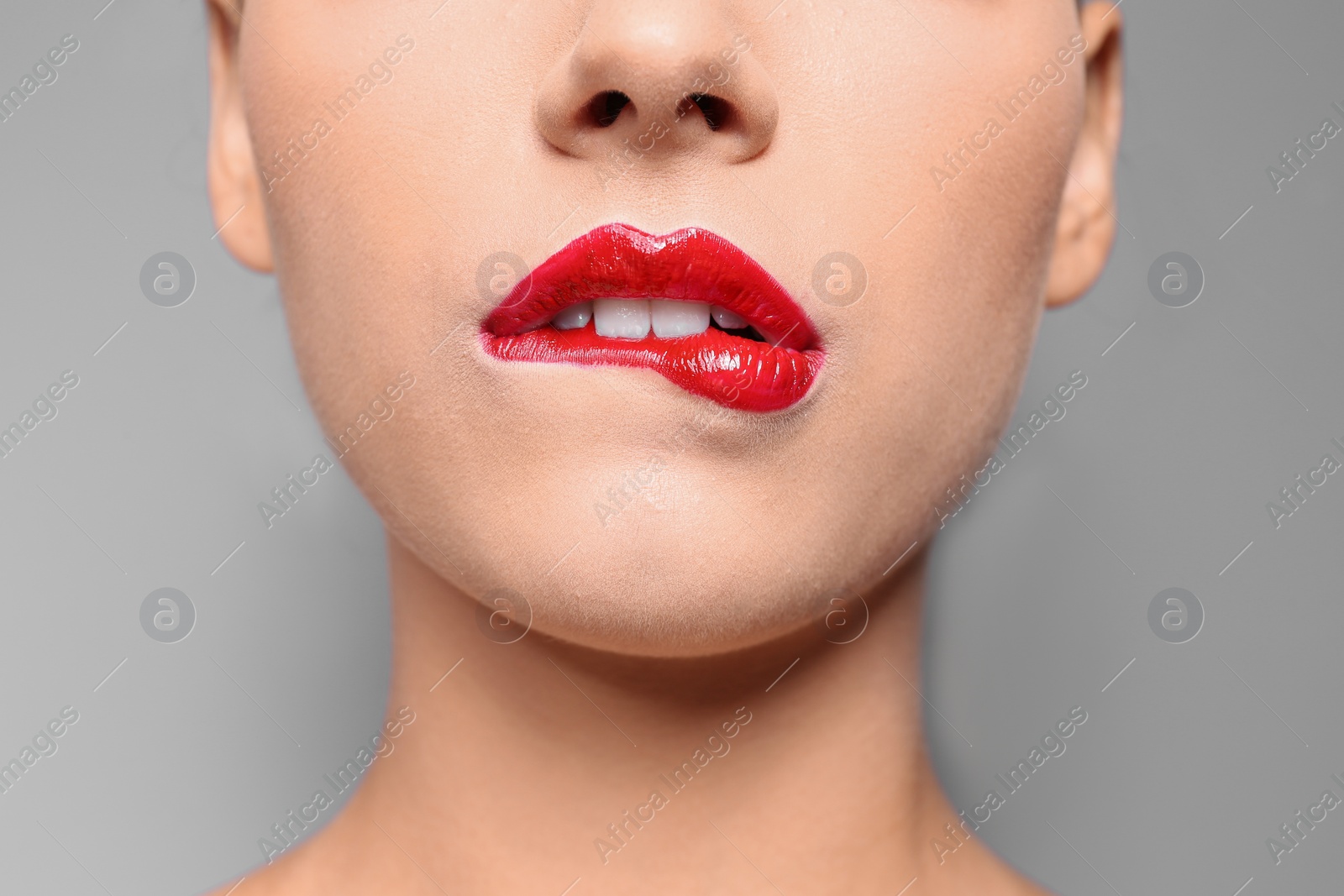 Photo of Beautiful young woman with red glossy lips on gray background, closeup