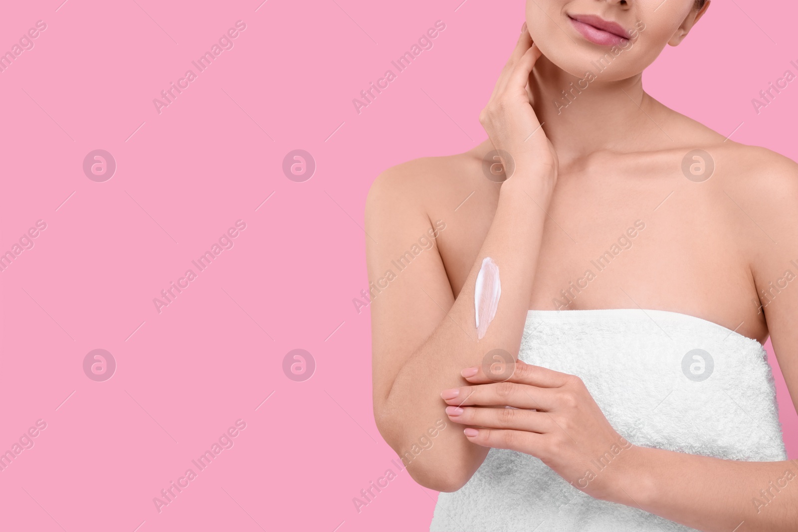 Photo of Woman with smear of body cream on her arm against pink background, closeup. Space for text