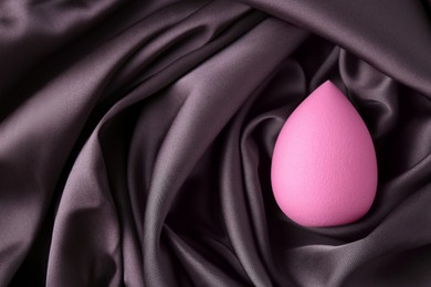 Pink makeup sponge on dark silk cloth, top view. Space for text