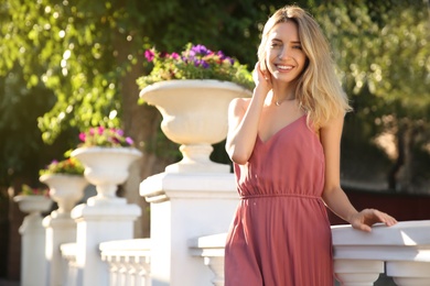 Beautiful young woman in stylish pink dress near vintage railing outdoors