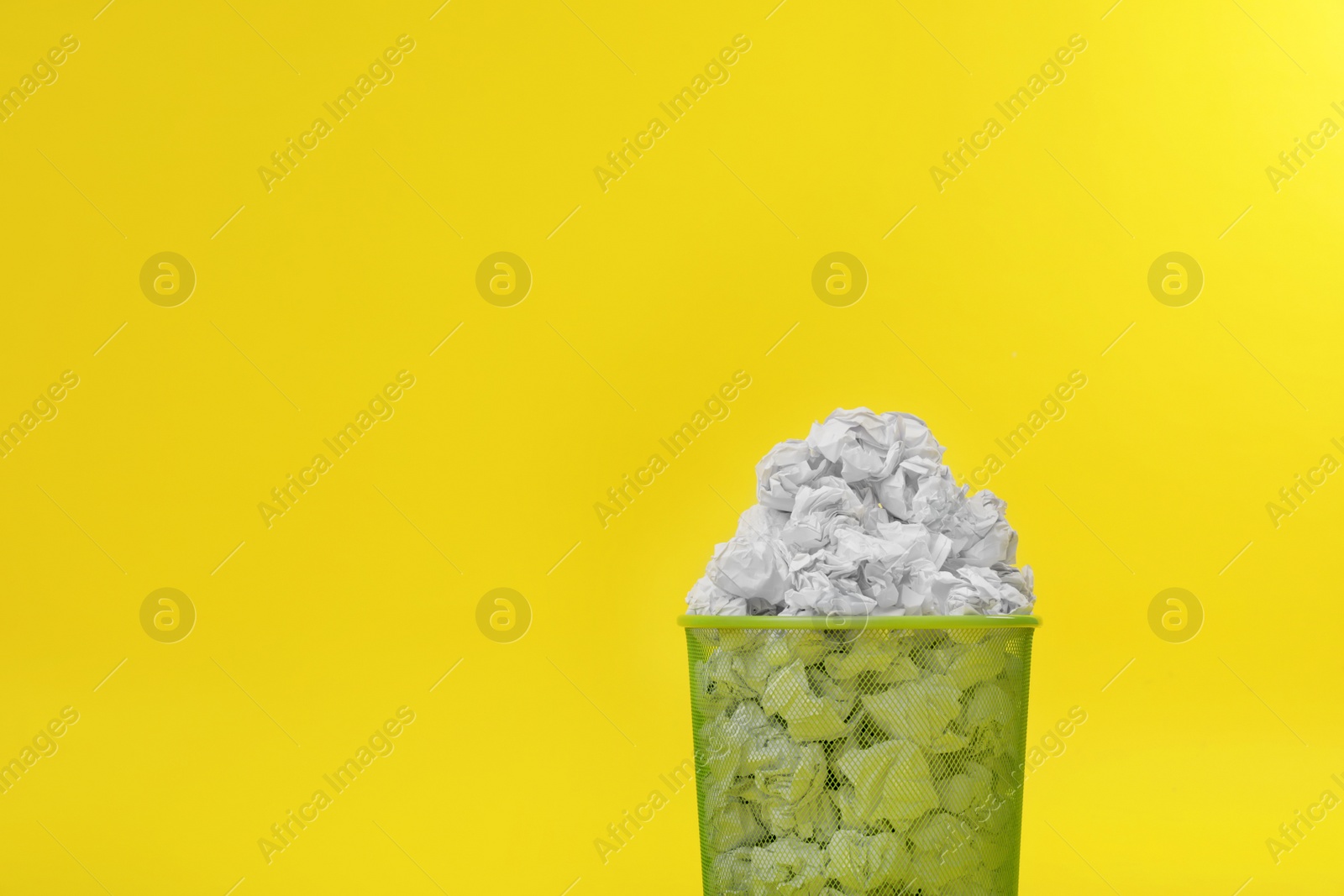 Photo of Metal bin with crumpled paper on color background, space for text