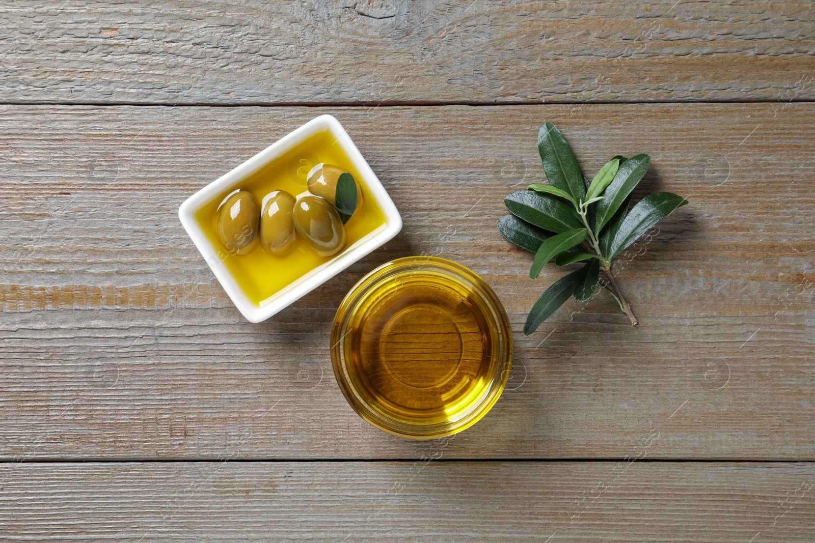 Photo of Fresh oil, ripe olives and green leaves on wooden table, flat lay