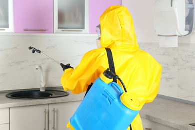 Pest control worker spraying pesticide in kitchen